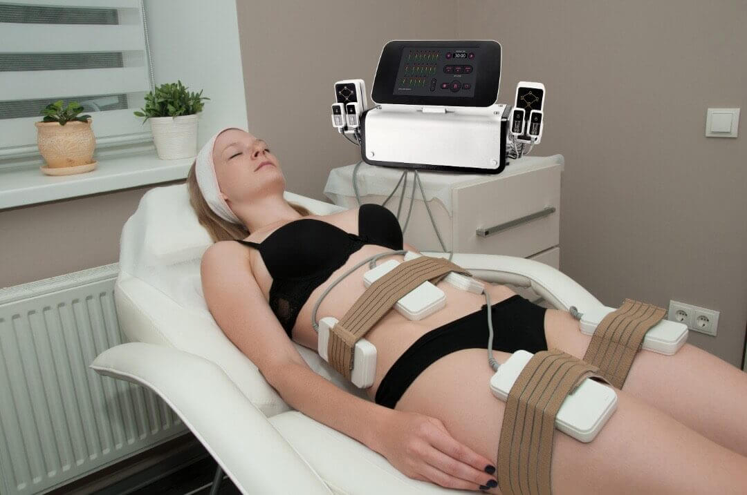 A woman receiving a non-invasive lipo laser treatment while lying on a spa bed, with multiple laser pads secured to her abdomen and thighs to target stubborn fat areas.